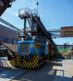 Die Dieselhydraulische Normalspur-Lokomotive Nr. 34, eine Henschel DHG 240 B  Esslinger , der Völklinger Hütte (ehem. Röchling'schen Eisen- und Stahlwerke GmbH in Völklingen/Saar, ab 1982 ARBED-Saarstahl GmbH, ab 1986 Saarstahl Völklingen GmbH) hier am 01 Juli 2025 abgestellt als Denkmal, mit zwei selbstentladende Schüttgutwagen der Gattung Fad oder Falns am Eingang der Rohstoffentladebunker in Richtung Hüttenbahnhof. Die Darstellung steht für den Rohstofftransport der Hütte zur Herstellung des Sintergutes. Die Lok war auch auf Bundesbahn Gleisen zugelassen. Heutiger Eigentümer der Lok und Wagen ist die Initiative Völklinger Hütte e.V..

Die zweiachsige dieselhydraulische Lok mit Antrieb über Gelenkwellen wurde 1969 von Henschel in Kassel unter der Fabriknummer 31210 gebaut und an die Röchling'sche Eisen- und Stahlwerke GmbH in Völklingen als Lok 34 geliefert. Weiterer Lebenslauf/Umfirmierungen: 
01.01.1971 > Stahlwerke Röchling-Burbach GmbH, Völklingen  34  
Juni 1982 	 > ARBED-Saarstahl GmbH, Völklingen  34  
Juni 1986 	 > Saarstahl Völklingen GmbH, Völklingen  34  
10.05.1989 > Saarstahl AG, Völklingen  34  
Später an MGS - Metallurgische Gesellschaft Saar mbH, Völklingen  34  
März 1999 	an Weltkulturerbe Völklinger Hütte - Europäisches Zentrum für Kunst und Industriekultur GmbH, Völklingen und Aufstellung als Denkmal. 

Die Lokomotive war bis zu einem Motorschaden 1997 in verschiedenen Bereichen eingesetzt: Transport von Duplexeisen zwischen der Mischerhalle und dem Siemens-Martin-Werk, im Bereich des Siemens-Martin-Werks, der Elektroöfen und des Hammerwerks sowie nach Einbau einer Funkfernsteuerung im Hafenbereich der Saarstahl AG.

Mit den Fahrzeugen der Typenreihe DHG 160 B / DHG 200 B / DHG 240 B und DHG 350 B bot Henschel Anfang der 1960er Jahre Gelenkwellenmaschinen für den unteren Leistungsbereich an, deren konstruktiver Ursprung nicht in Kassel, sondern in Esslingen der lag. Im Jahr 1961 übernahm Henschel das Diesellok-Typenprogramm der Maschinenfabrik Esslingen. Es wurde eine bei der Maschinenfabrik Esslingen als Typ Bern in Auftrag gegebene Lokomotive als DHG 325 in Kassel fertig gebaut und an den Auftraggeber, die Duisburger Kupferhütte, ausgeliefert. Der Typ Bern stellte auch die Basis für das oben genannte Typenprogramm dar. Dieses unterschied sich zwar optisch deutlich von seinem Esslinger Ursprung, übernahm aber die wesentlichen konstruktiven Merkmale der Fahrzeuge aus Esslinger Produktion. Gleichzeitig gab es keinen technischen und optischen Bezug zu den bisher im eigenen Henschel-Typenprogramm angebotenen Fahrzeugen.

Bei den neuen Gelekwellenfahrzeugen gab es leistungsmäßig deutliche Überschneidungen mit dem kleinsten Typ der 3. Generation, der stangengetriebenen DH 240 B. Diese wurde dann in der 4. Generation durch die DHG 240 B ersetzt.

Die Henschel DHG 240 B wurde zwischen 1963 und 1971 in 34 Exemplaren gebaut. Die Loks gingen vornehmlich an Chemiebetriebe und Raffinerien in Deutschland und der Schweiz. Von diesen wurden elf Loks explosionsgeschützt ausgerüstet. Einzelne Loks wurden ebenfalls mit Funkfernsteuerung ausgerüstet. Mit weitem Abstand am stückzahlenstärksten ist die DHG 240 B, die im Gegensatz zu ihren schwächeren  Schwestern  nicht mit einem DIWABUS-Getriebe von Henschel, sondern mit einem Voith-Hydraulikgetriebe ausgestattet ist. Zahlreiche Fahrzeuge stehen auch heute noch im täglichen Einsatz.

TECHNISCHE DATEN:
Baujahre: 1963 bis 1971
Gebaute Stückzahl: 34
Spurweite:	1.435 mm (Normalspur)
Achsfolge: B
Länge über Puffer: 7.160 mm
Achsabstand: 2.800 mm
größte Breite: 3.000 mm
größte Höhe über Schienenoberkante: 3.600 mm
Raddurchmesser: 850 mm (neu)
kleinster befahrbarer Gleisbogen: 35 m
Eigengewicht: 28 t
Max. Achslast: 16 t
Dieselmotor: wassergekühlter 6 Zylinder / 4-Takt-Diesel-Reihenmotor mit Turboaufladung, ohne Ladeluftkühlung vom Typ Henschel 6R 1416 A, Hubraum 13,3 l.
Leistung: 177 kW (240 PS)
Drehzahl: 1.600 U/min
Höchstgeschwindigkeit: 30 / 60 km/h
Leistungsübertragung: hydraulisch (Voit-Getriebe)
Kraftstoffvorrat: 400 l
