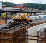 Mal ein Blick über den Teleskopausleger.  
Nun im Einsatz der 125 t KIROW Gleisbauschienenkran KIROW Multi Tasker KRC 810 T (mit Schwerlastausrüstung), Schweres Nebenfahrzeug Nr. D-HGUI 99 80 9419 024-1, ex 97 82 53 513 19-3, der HERING Bahnbau GmbH (Burbach) ist am 29 September 2025 im Betzdorf/Sieg. 

Hier im Bereich unter dem P+R Parkhaus bis zum Fluss Sieg werden Horizontalbohrungen gemacht, vermutlich für erforderliche Entwässerungs-Leitungen. So mussten Bohrrohre in die Baugrube gehoben werden und wie hier der Abraum aus der Baugrube gehoben werden. Eigentlich ist ein 125 t Kran damit unterfordert (überdimensioniert), aber man muss bedenken es wurde eine weite Auskragung (Ausladung vor Puffer) und das freistehend (Nichtabgestützt) benötigt. 

Der hier mit der Ausladung vor Puffer von über 15 m könnte der Kran freistehend 30 t heben, aber darf dann nicht schwenken. Wenn geschenkt werden muss liegt diese dann nur bei 1,5 t. Entscheidend für die Ausladung des Auslegers ist aber auch die hintere Ausladung des Gegengewichts
