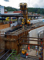 Nun im Einsatz der 125 t KIROW Gleisbauschienenkran KIROW Multi Tasker KRC 810 T (mit Schwerlastausrüstung), Schweres Nebenfahrzeug Nr. D-HGUI 99 80 9419 024-1, ex 97 82 53 513 19-3, der HERING Bahnbau GmbH (Burbach) ist am 29 September 2025 im Betzdorf/Sieg. 

Hier im Bereich unter dem P+R Parkhaus bis zum Fluss Sieg werden Horizontalbohrungen gemacht, vermutlich für erforderliche Entwässerungs-Leitungen. So mussten Bohrrohre in die Baugrube gehoben werden und wie hier der Abraum aus der Baugrube gehoben werden. Eigentlich ist ein 125 t Kran damit unterfordert (überdimensioniert), aber man muss bedenken es wurde eine weite Auskragung (Ausladung vor Puffer) und das freistehend (Nichtabgestützt) benötigt. 

Der hier mit der Ausladung vor Puffer von über 15 m könnte der Kran freistehend 30 t heben, aber darf dann nicht schwenken. Wenn geschenkt werden muss liegt diese dann nur bei 1,5 t. Entscheidend für die Ausladung des Auslegers ist aber auch die hintere Ausladung des Gegengewichts. 