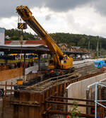 Nun im Einsatz der 125 t KIROW Gleisbauschienenkran KIROW Multi Tasker KRC 810 T (mit Schwerlastausrüstung), Schweres Nebenfahrzeug Nr. D-HGUI 99 80 9419 024-1, ex 97 82 53 513 19-3, der HERING Bahnbau GmbH (Burbach) ist am 29 September 2025 im Betzdorf/Sieg. 

Hier im Bereich unter dem P+R Parkhaus bis zum Fluss Sieg werden Horizontalbohrungen gemacht, vermutlich für erforderliche Entwässerungs-Leitungen. So mussten Bohrrohre in die Baugrube gehoben werden und wie hier der Abraum aus der Baugrube gehoben werden. Eigentlich ist ein 125 t Kran damit unterfordert (überdimensioniert), aber man muss bedenken es wurde eine weite Auskragung (Ausladung vor Puffer) und das freistehend (Nichtabgestützt) benötigt. 

Der hier mit der Ausladung vor Puffer von über 15 m könnte der Kran freistehend 30 t heben, aber darf dann nicht schwenken. Wenn geschenkt werden muss liegt diese dann nur bei 1,5 t. Entscheidend für die Ausladung des Auslegers ist aber auch die hintere Ausladung des Gegengewichts. 